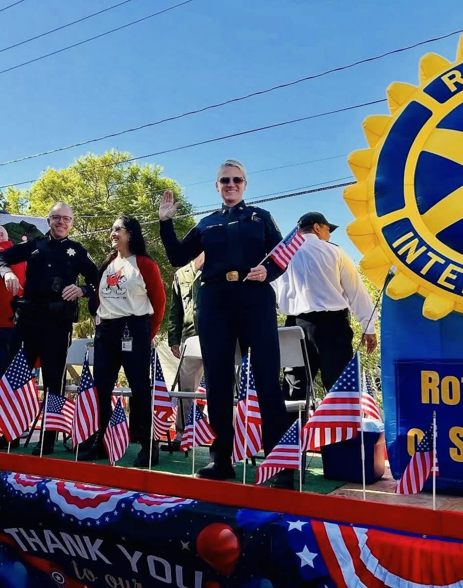 A parade with people holding a red banner that reads 'TAI JI MEN QIGONG ACADEMY' in English and Chinese, with a dragon dance performance, people dressed in white traditional clothing, and a dragon costume moving down a city street.