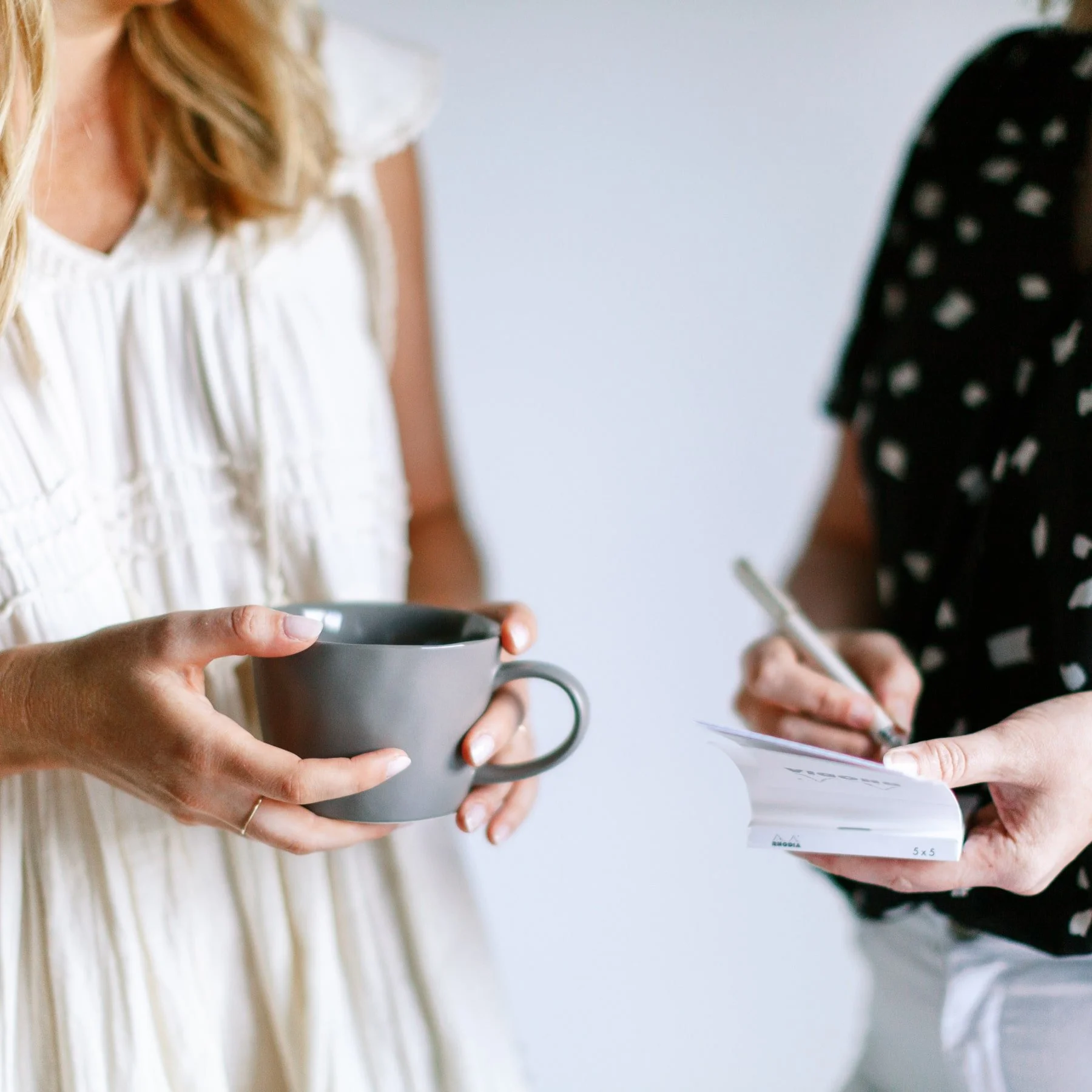 two women talking while one takes notes and other drinks coffee