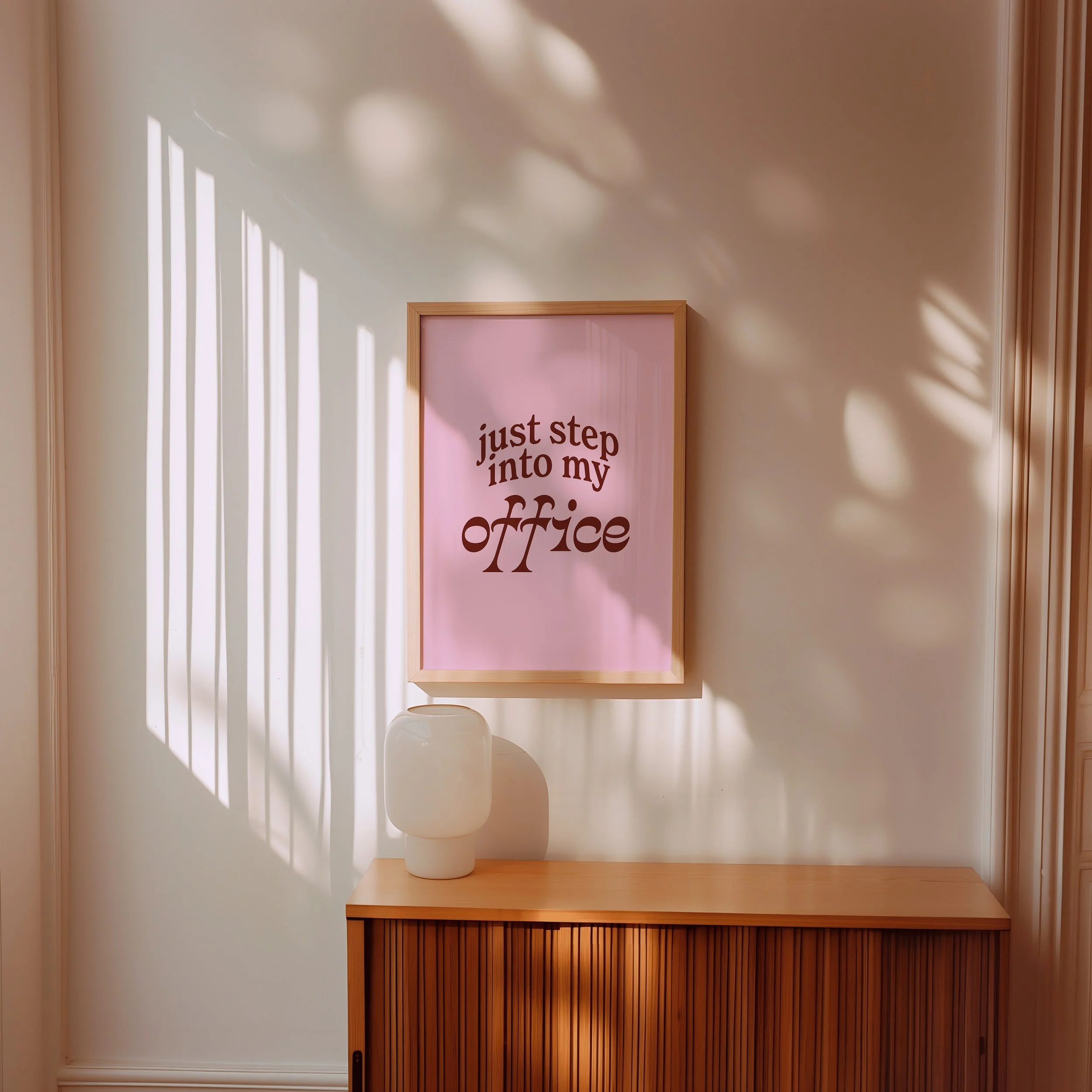 A partially opened wooden cabinet door reveals an interior shelf with a pink sign that reads 'just step into my office' and a white jar or container on top. The background wall features shadow patterns from window blinds.