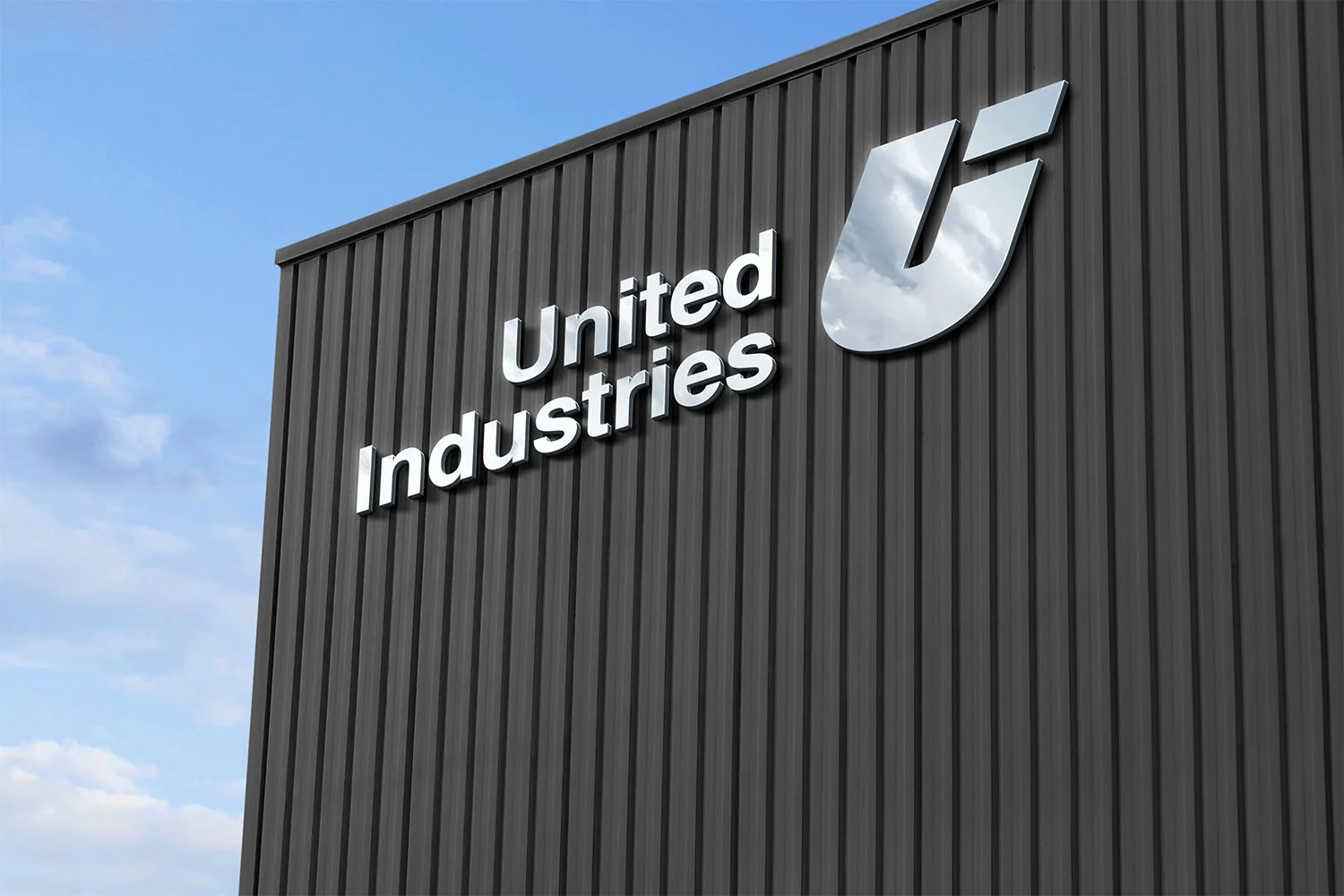 The exterior of a building with the United Industries logo and name on a dark gray corrugated metal wall against a blue sky with some clouds.