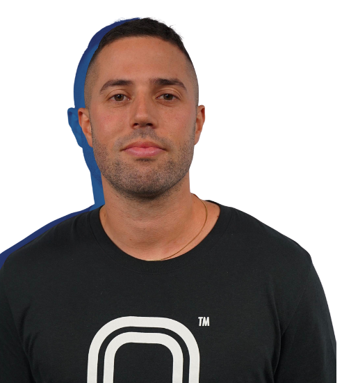A young man with short dark hair, light skin, and a slight beard, wearing a black t-shirt with a white logo, standing against a plain background.