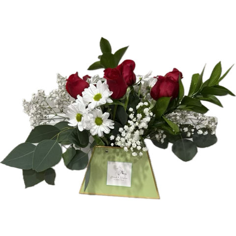 A floral arrangement with white roses, baby's breath, and white chrysanthemums in a pink flower box on a white round table.