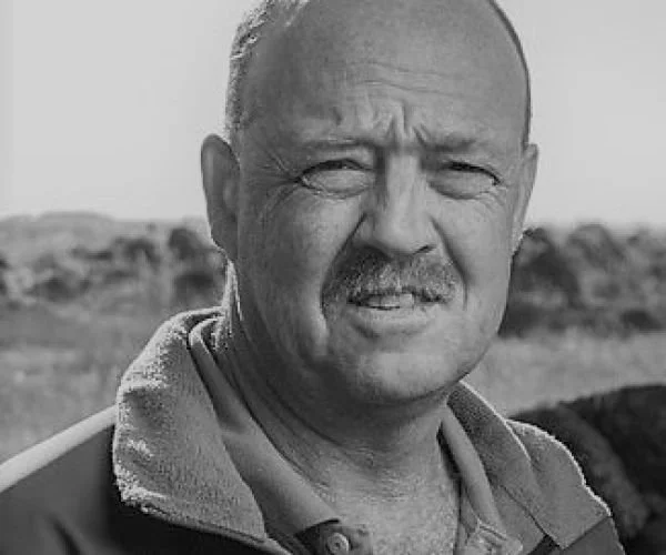 Black and white photo of a man with a mustache and short hair, outdoors in a rural or open landscape.