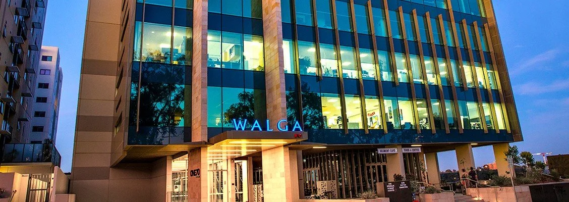 Modern office building with glass windows and illuminated interior, with a blue 'WALGA' sign on the front.