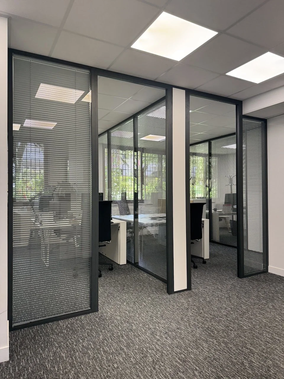 Bureaux avec diviseures en verre avec volets roulants, mobilier de bureau et vue extérieure avec arbres