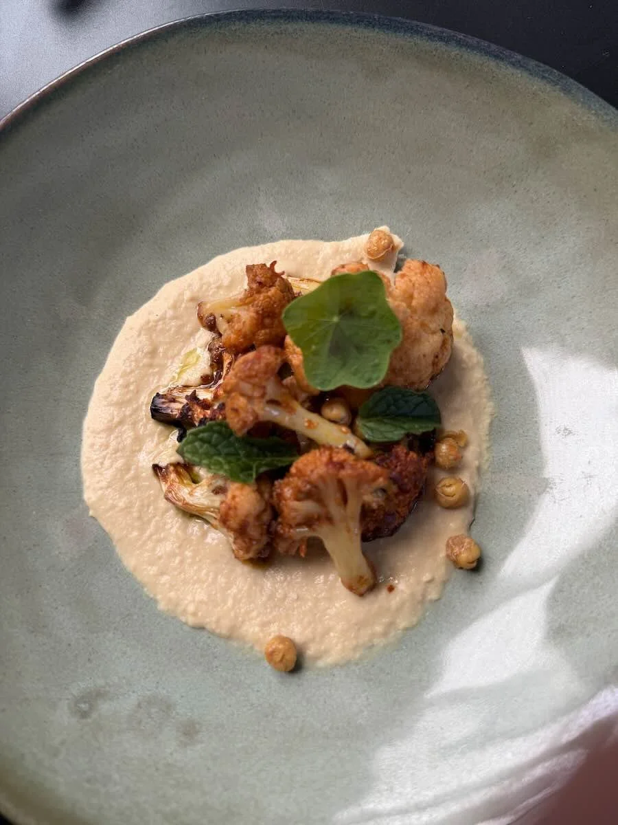Deeply roasted cauliflower paired with harissa, smooth hummus, and crispy fried chickpeas for texture