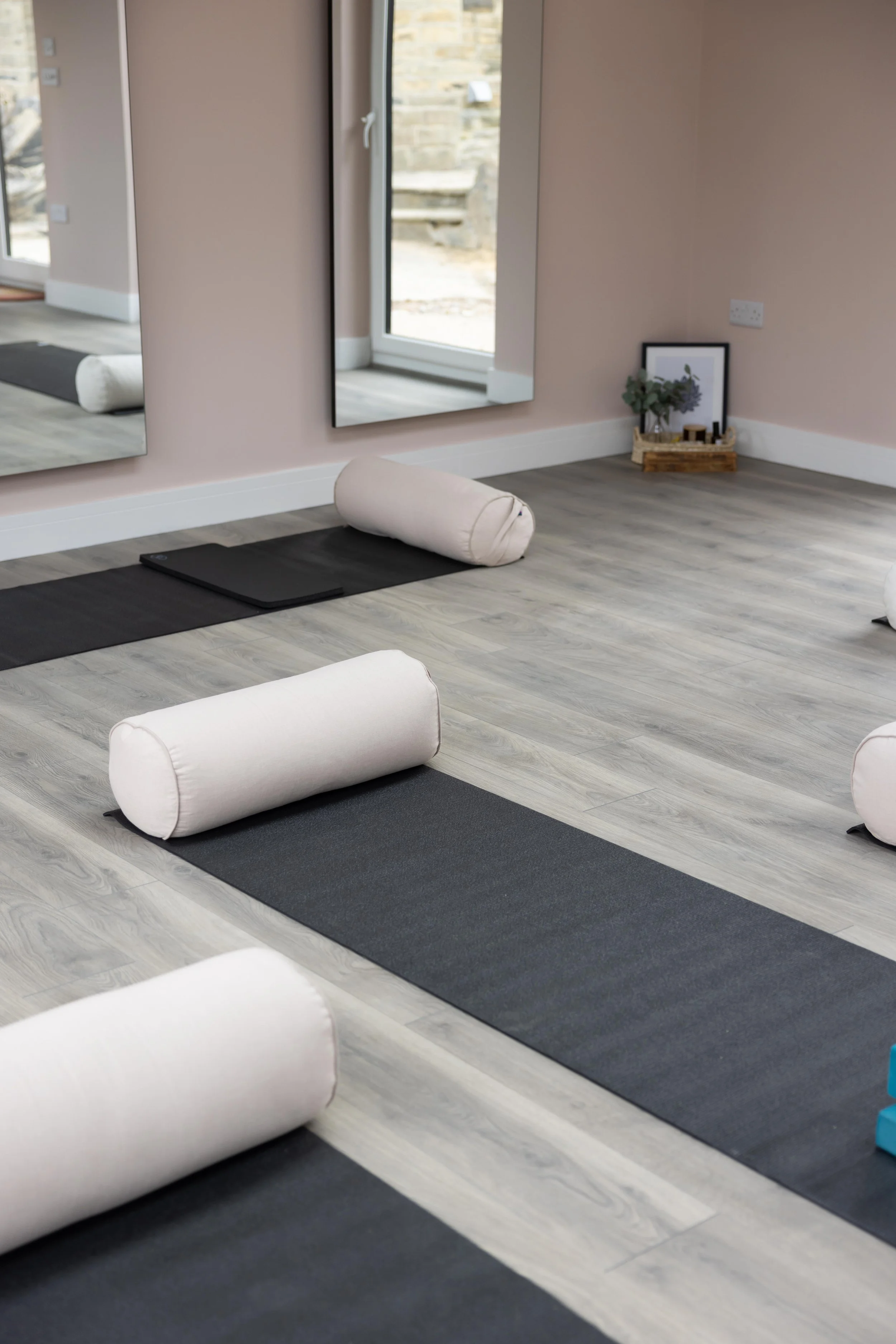 Yoga studio interior with black mats, cream bolsters, and large mirrors on the wall.