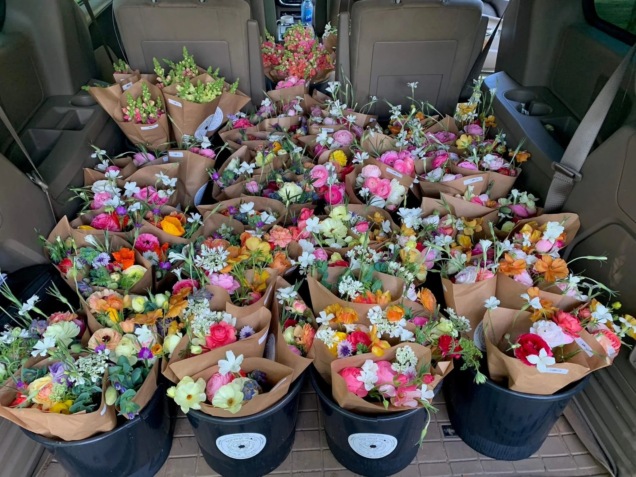 Multiple buckets filled with colorful flower bouquets, placed inside a vehicle.