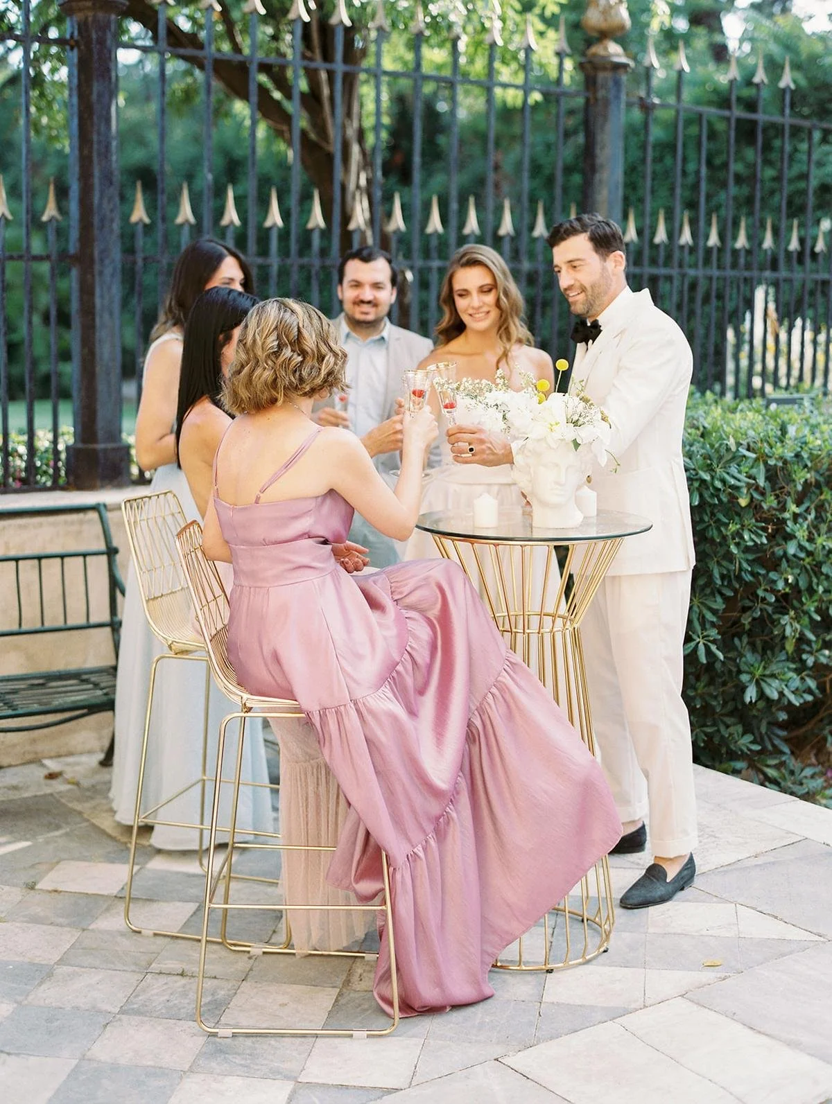 People at a wedding reception raising glasses for a toast outdoors, with a bride in a white dress and a groom in a white tuxedo.
