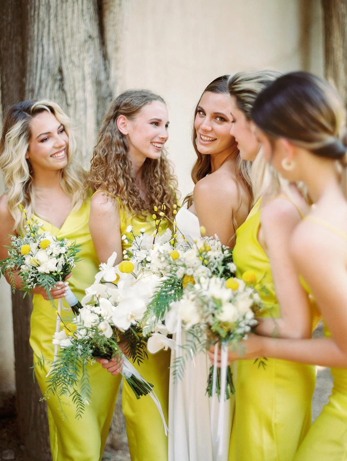 A group of women in yellow dresses at a wedding, holding bouquets and smiling.