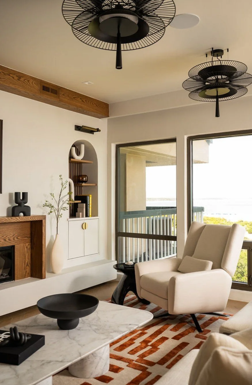 Modern living room with beige armchair, white marble coffee table, decorative black bowl, large sliding glass door, and unique black ceiling fans