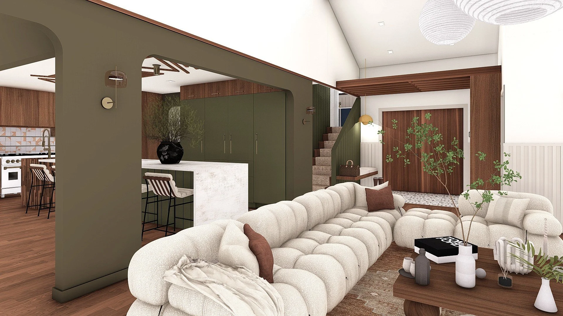 Living room with a large, white, tufted sectional sofa, brown and beige throw pillows, and a wooden coffee table with vases and books. A potted plant and a wooden accent wall with sliding door are in the background, with a staircase and green cabinetry visible.