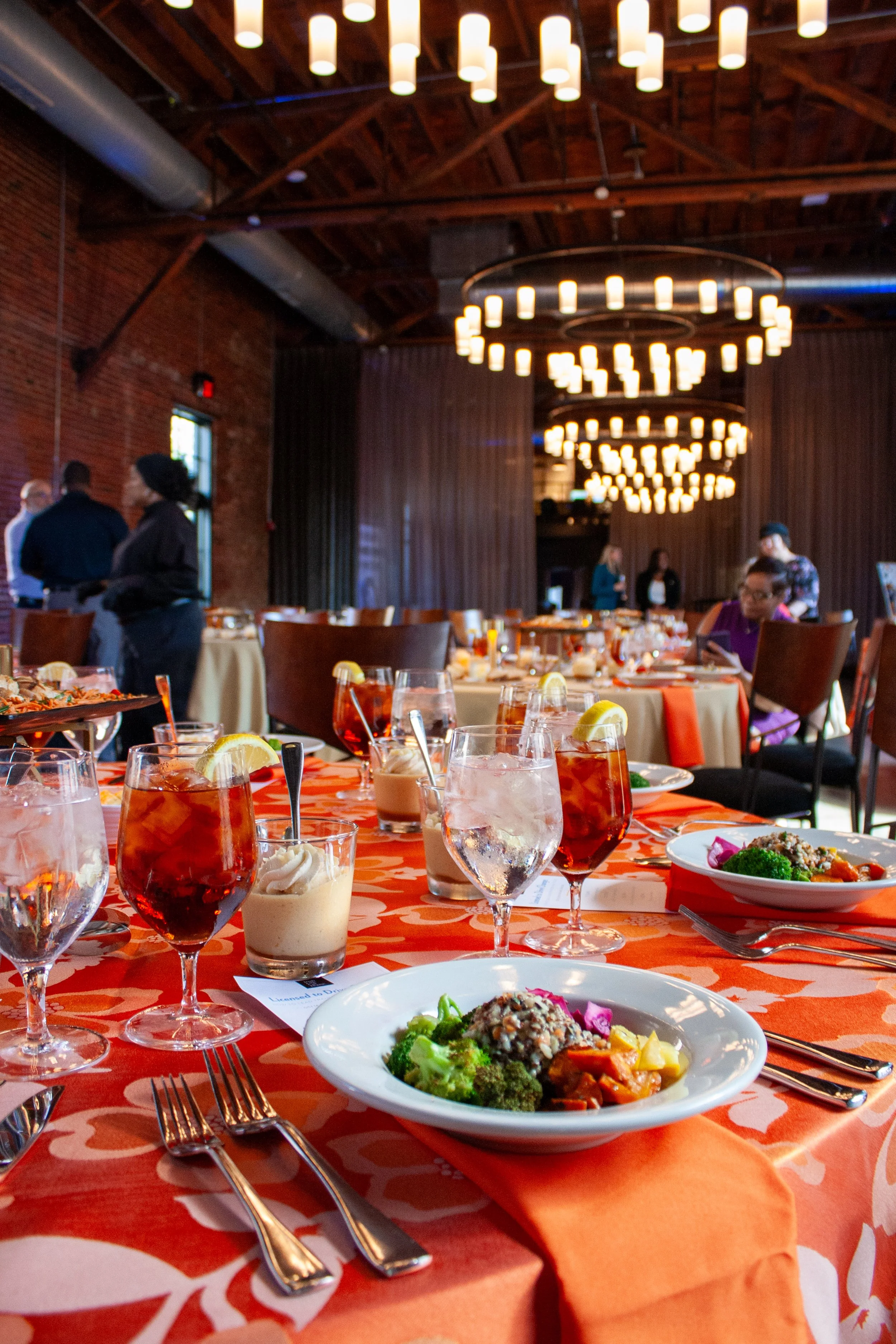 A round table with an orange linen is set with a bowl of rice and colorful veggies by Together & Company catering. Guests await a lunch and learn presentation in a spacious historic event venue in German Village, Columbus, Ohio.