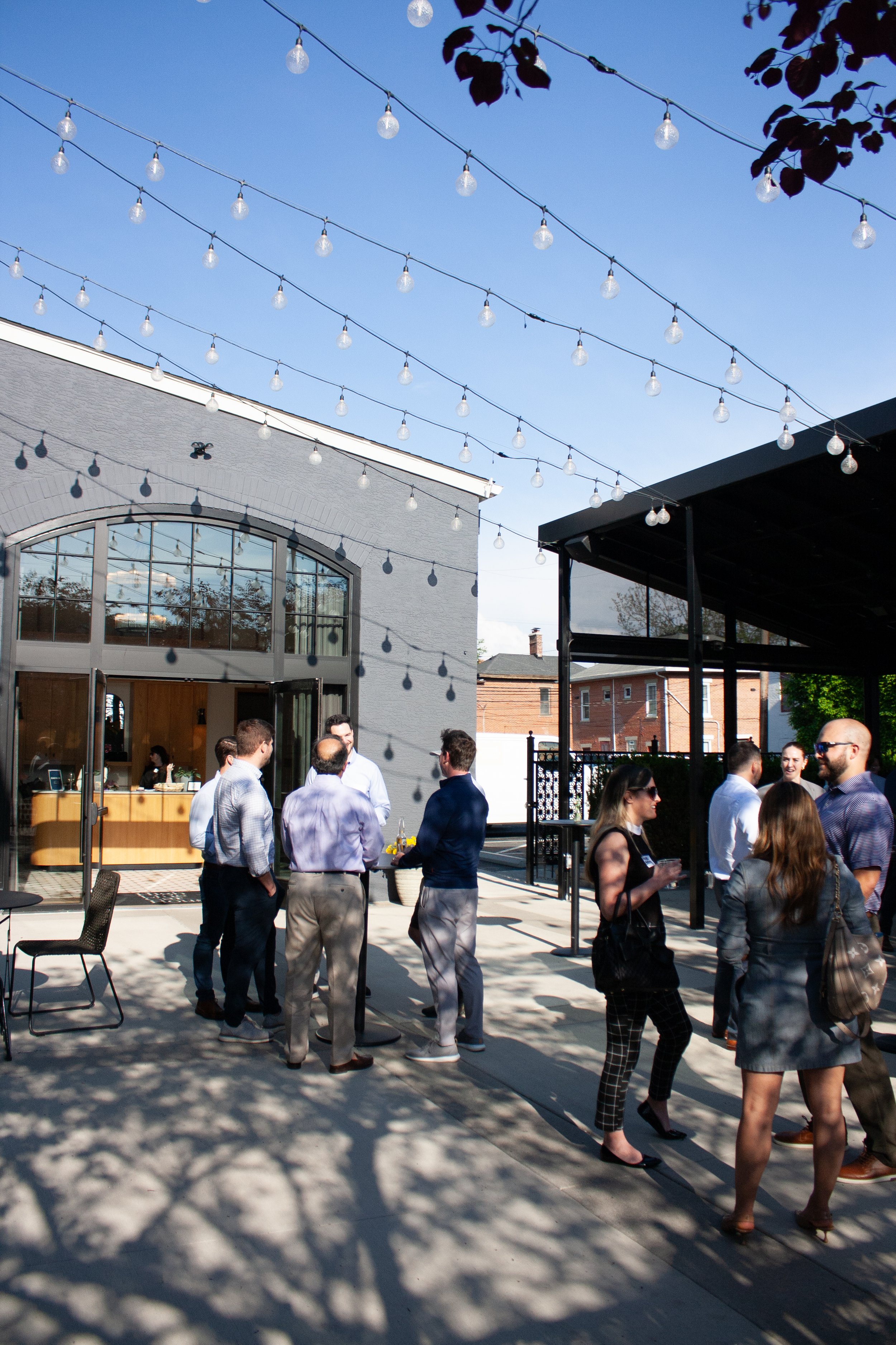 The outdoor patio space at High Line Car House is in full swing for a weekday corporate happy hour. Guests enjoy their drinks underneath Edison lights that are strung between the venue and the covered pergola.