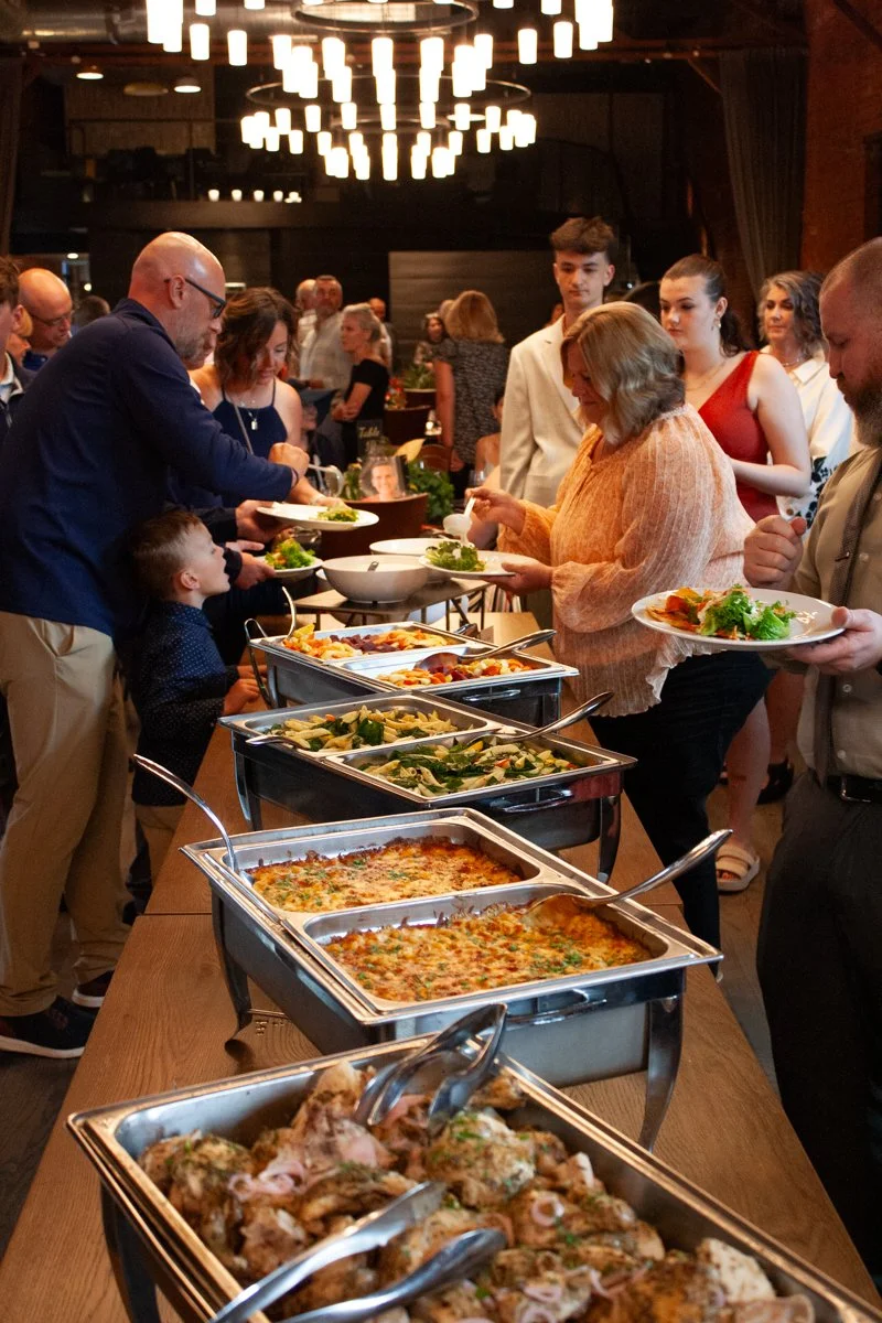 Event guests line up at a long buffet table filled with Together & Company catering at a nonprofit dinner fundraiser in a historic industrial event space in Columbus, Ohio