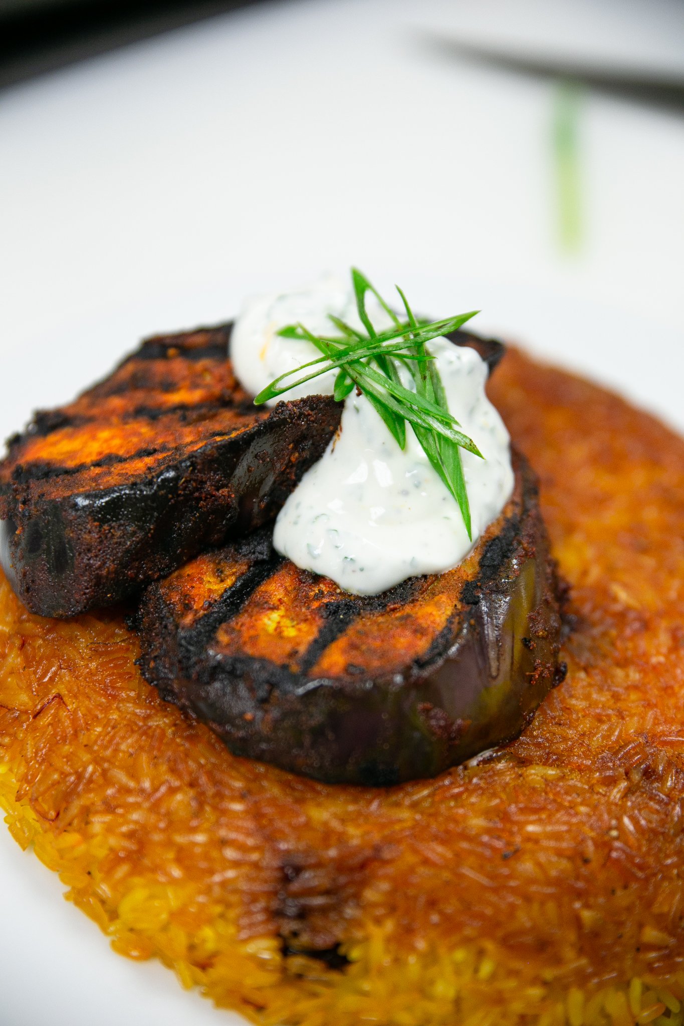  A vegetarian wedding dish, grilled eggplant, is plated atop a bed of fried rice and garnished with a tzatziki sauce and scallions.  