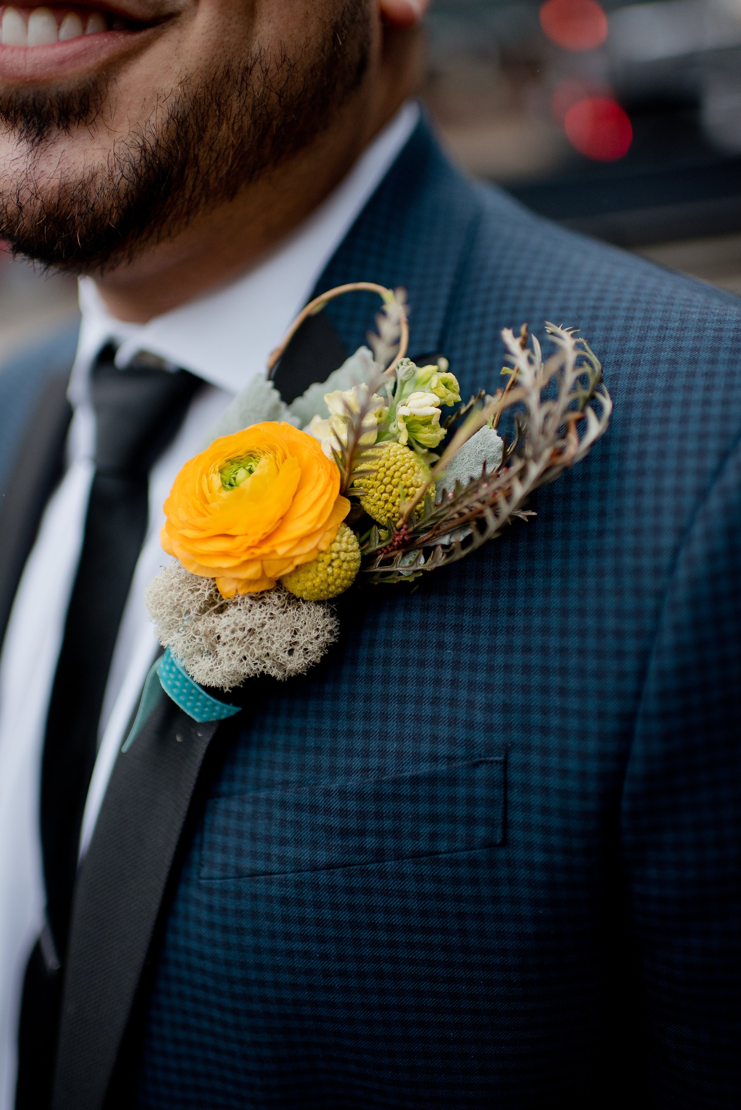  The closeup of a groom’s boutonniere, adorned with golden flowers and textured greenery.  