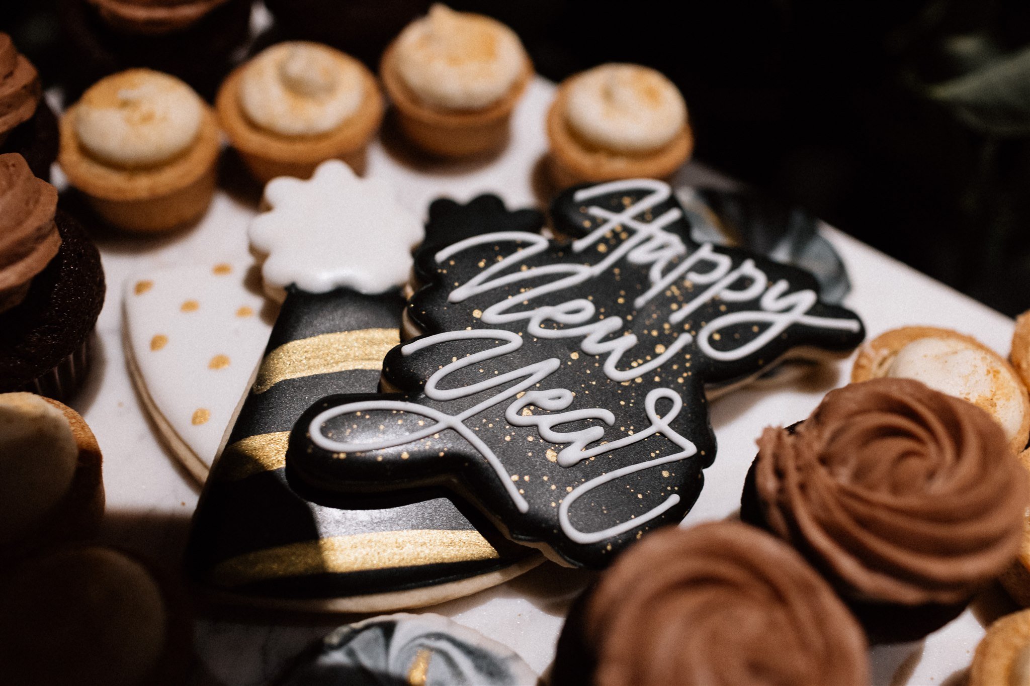  A closeup of a wedding cookie tray; one of the cookies reads “Happy New Year” in royal icing. 