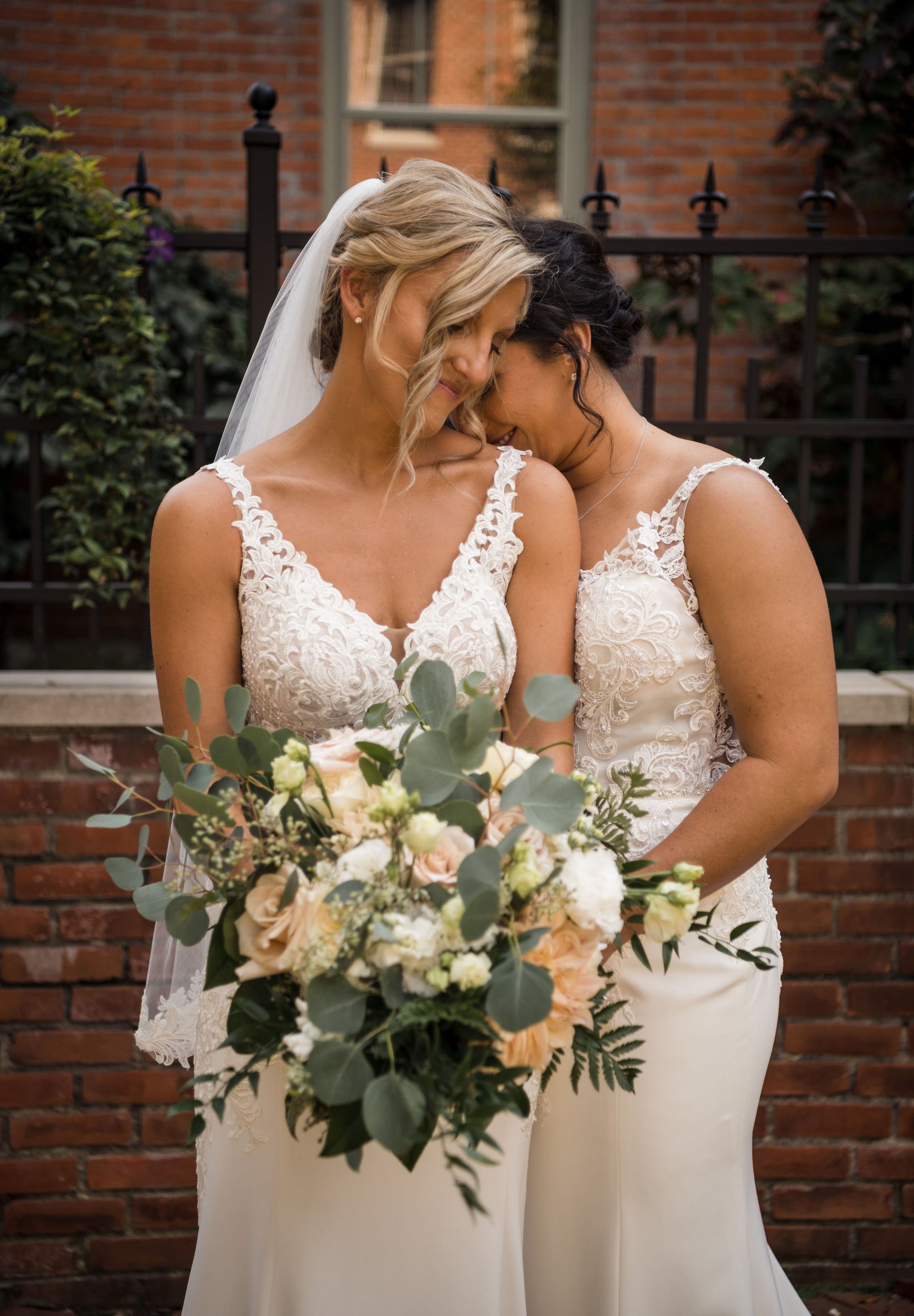  Two brides lean in together for a photo in a romantic courtyard before their wedding ceremony in Columbus, Ohio. 