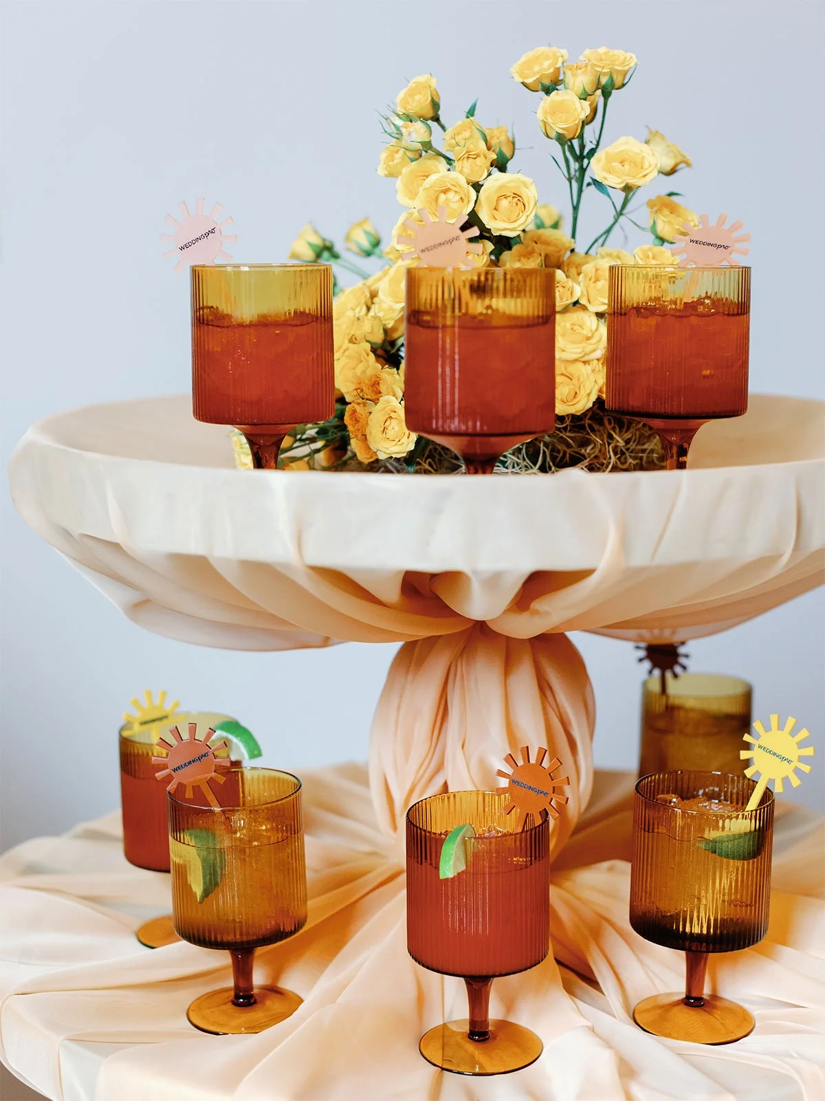 A custom cocktail is in short orange goblets on a multi-tiered stand draped with orange fabric.