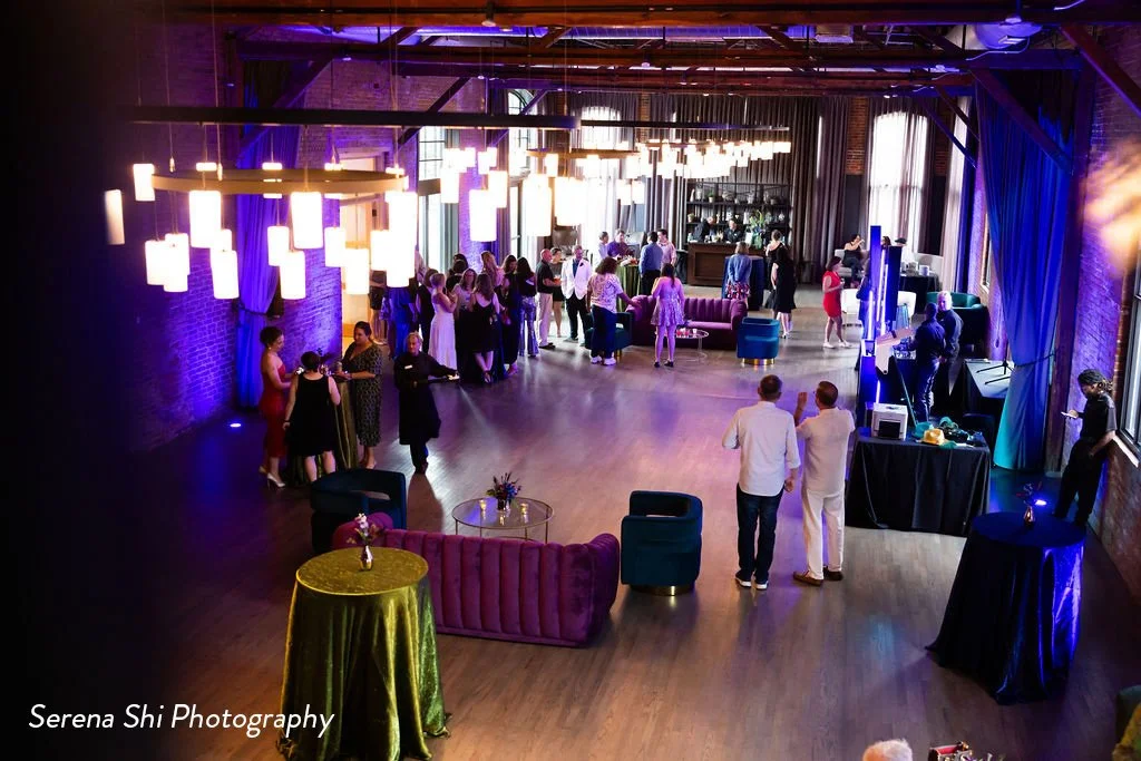 An overhead view of a birthday party event at High Line Car House, with purple uplighting, plush furniture, and green and blue linen accents.