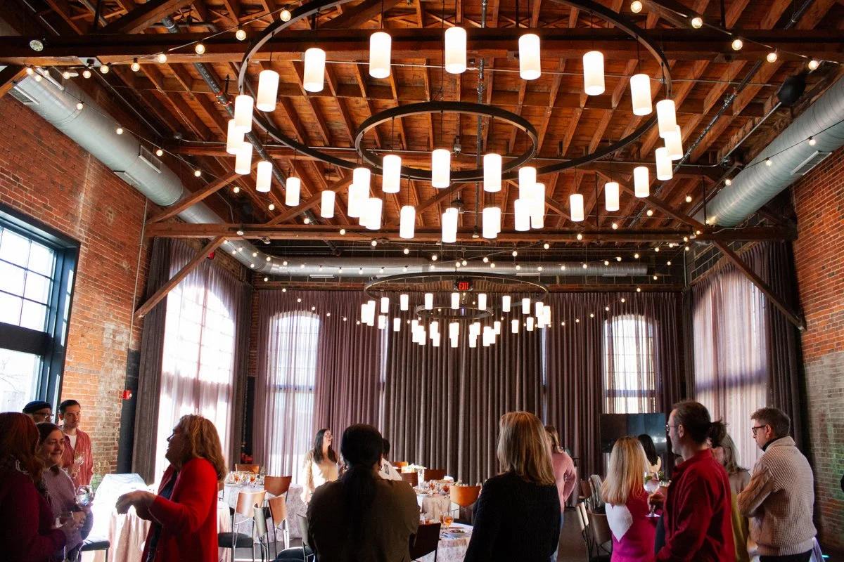 Exposed beams and contemporary chandeliers above a daytime corporate event at High Line Car House, an event venue in Columbus, Ohio.
