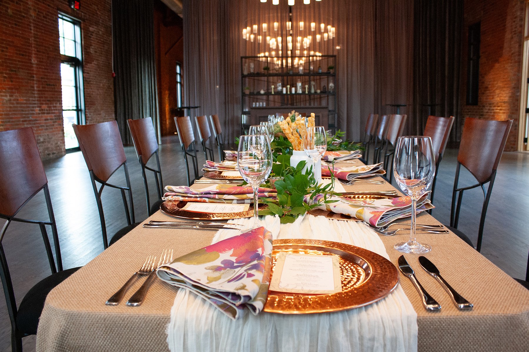 A long, banquet table is set for a private dinner party at High Line Car House in Columbus, Ohio. Curtains are drawn closed halfway through the room to make the event space feel smaller and more intimate. 