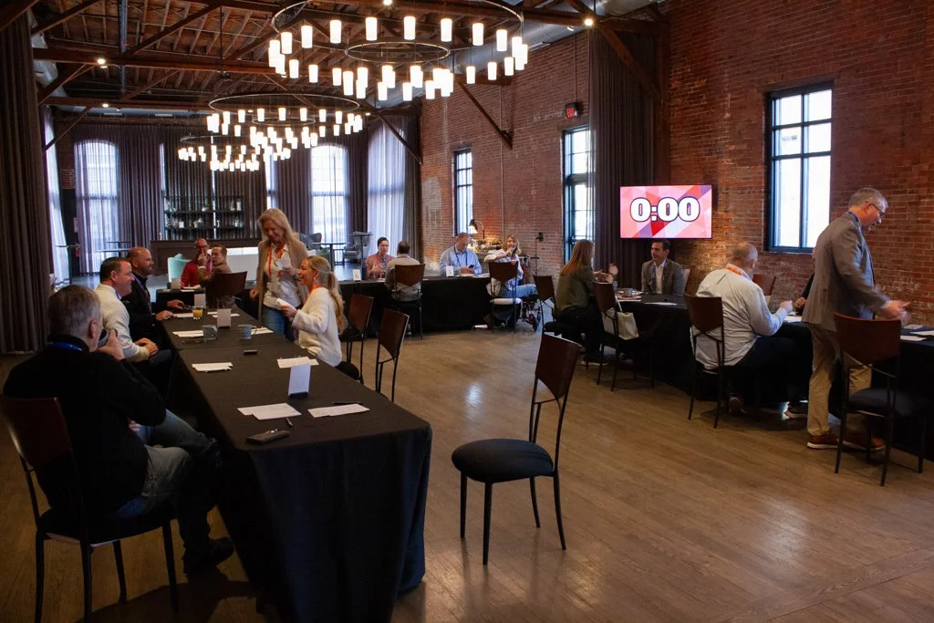 Long tables are set up in a horseshoe shape in a spacious event venue for a morning corporate meet-and-greet in Columbus, Ohio. Guests sit across from each other along the table to chat and network.