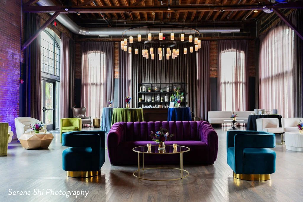 An arrangement of colorful blue, green, and purple rental furniture fills a spacious, industrial event space in downtown Columbus, Ohio.