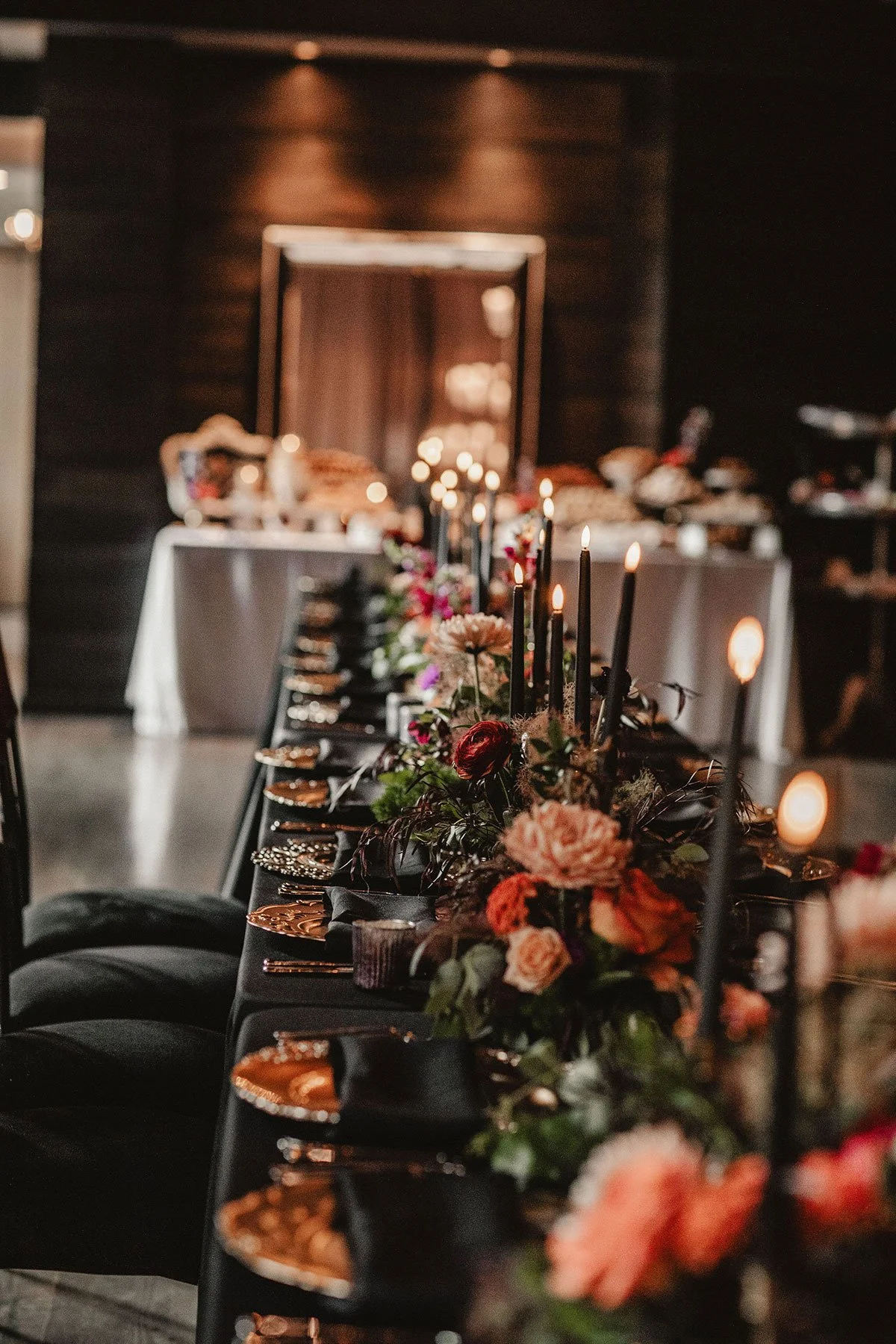 A long table is decorated for a wedding reception in Columbus, Ohio with black linen and napkins, metallic chargers, autumnal florals, and black candlesticks.