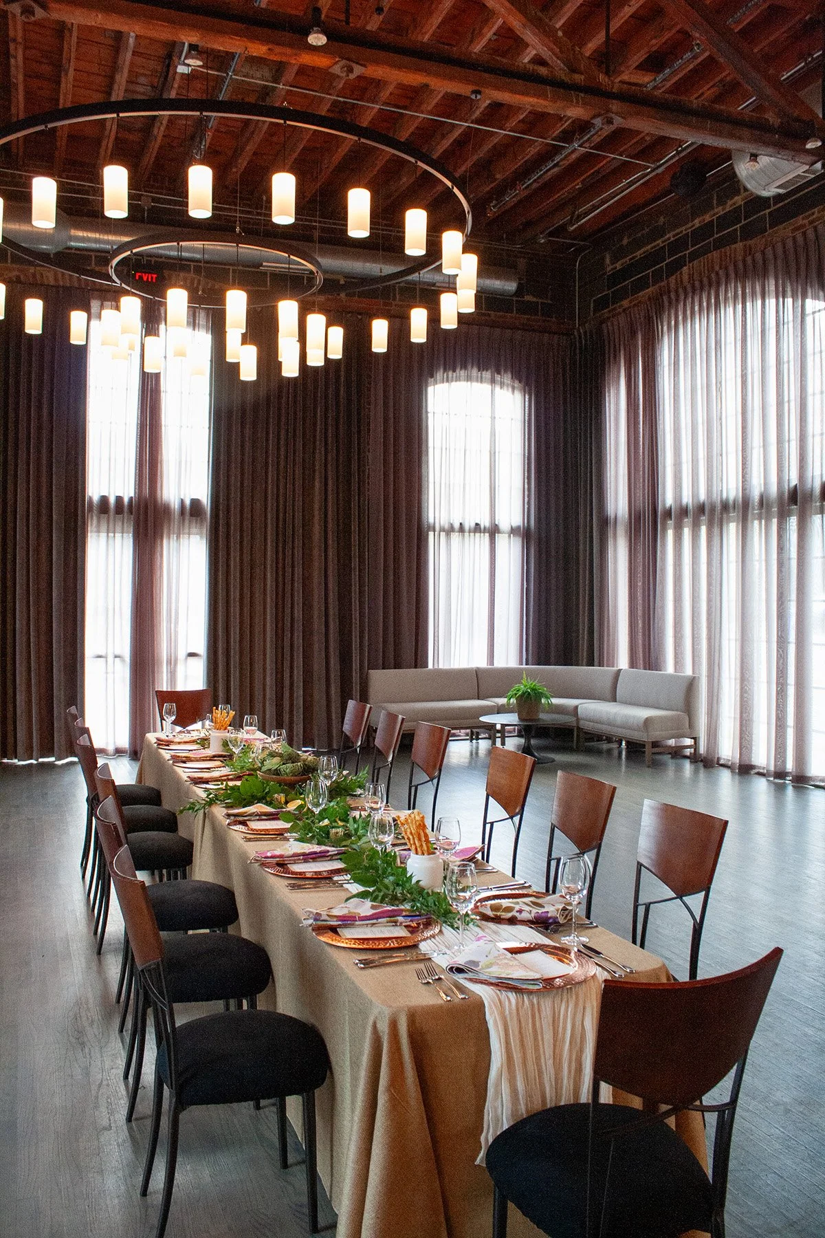A long table is set up for a small celebration dinner in an industrial event space with tall windows in Columbus, Ohio.