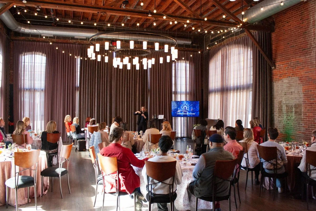 Event guests attend a lunch and learn in the High Line Car House grande hall. Cafe lights are strung above the event space. 