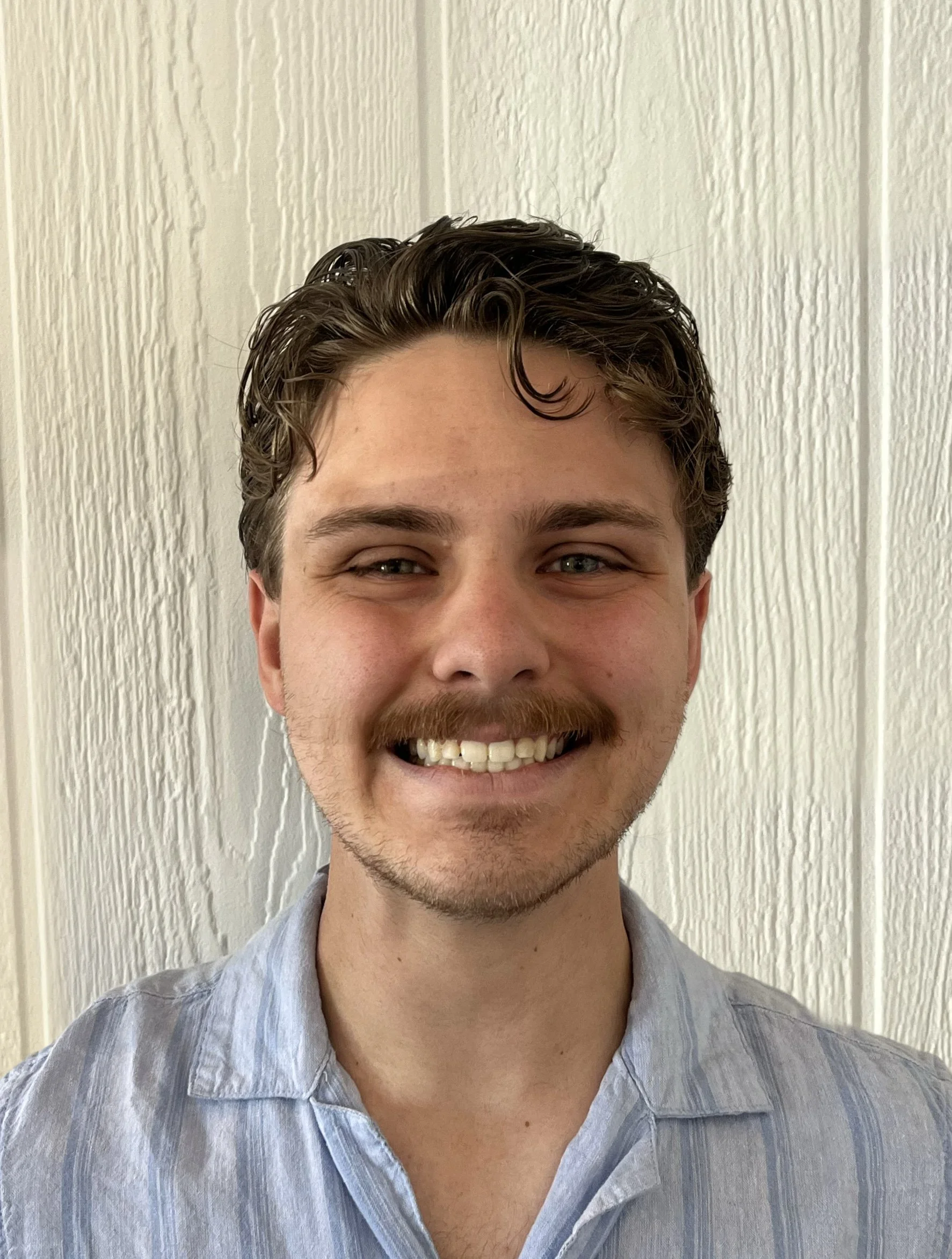 Young woman smiling with long brown hair and pearl earrings in an indoor setting.