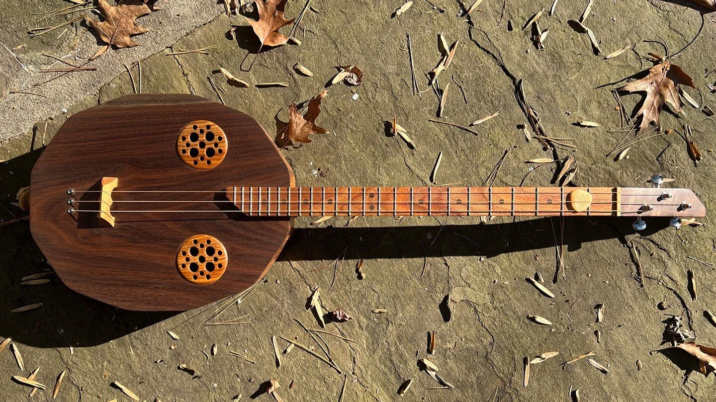 This acoustic/electric, uniquely shaped three string guitar is made with beautiful walnut and canary woods. #woodworking #cigarboxnation #cigarboxguitar #acoustic #acousticelectric #folkguitar #acousticguitar #walnutwood #homemadeguitar