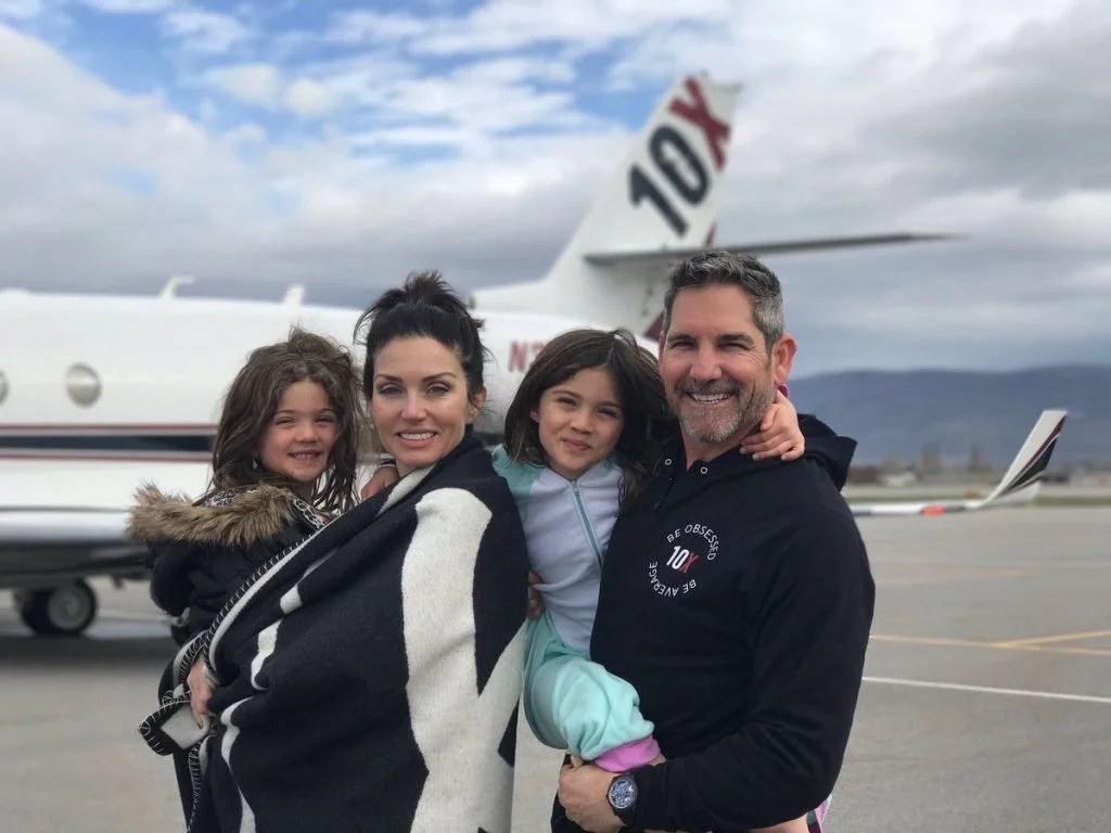 Family of four smiling and hugging in front of a private jet on an airport tarmac.