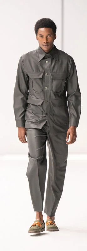 Model wearing a gray button-up shirt and matching pants with loafers on a runway.