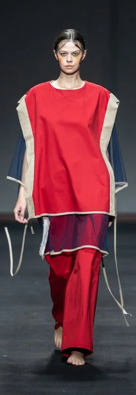 Model wearing a loose red and beige outfit on the runway.