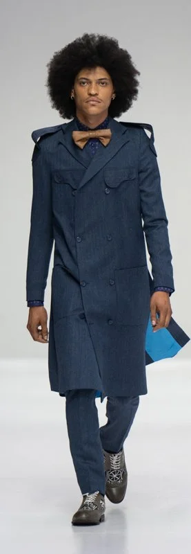 Model wearing a long blue coat with a bow tie on a runway.