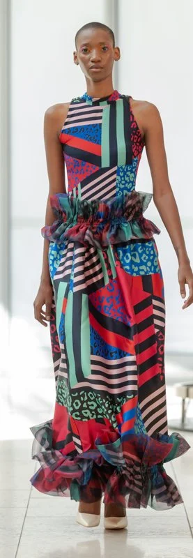 Model wearing colorful, patterned dress with ruffled details and high neckline on runway