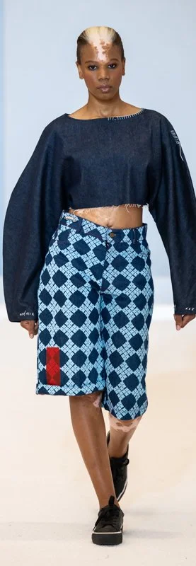 Model on runway wearing dark blue cropped top and blue patterned skirt with red accent