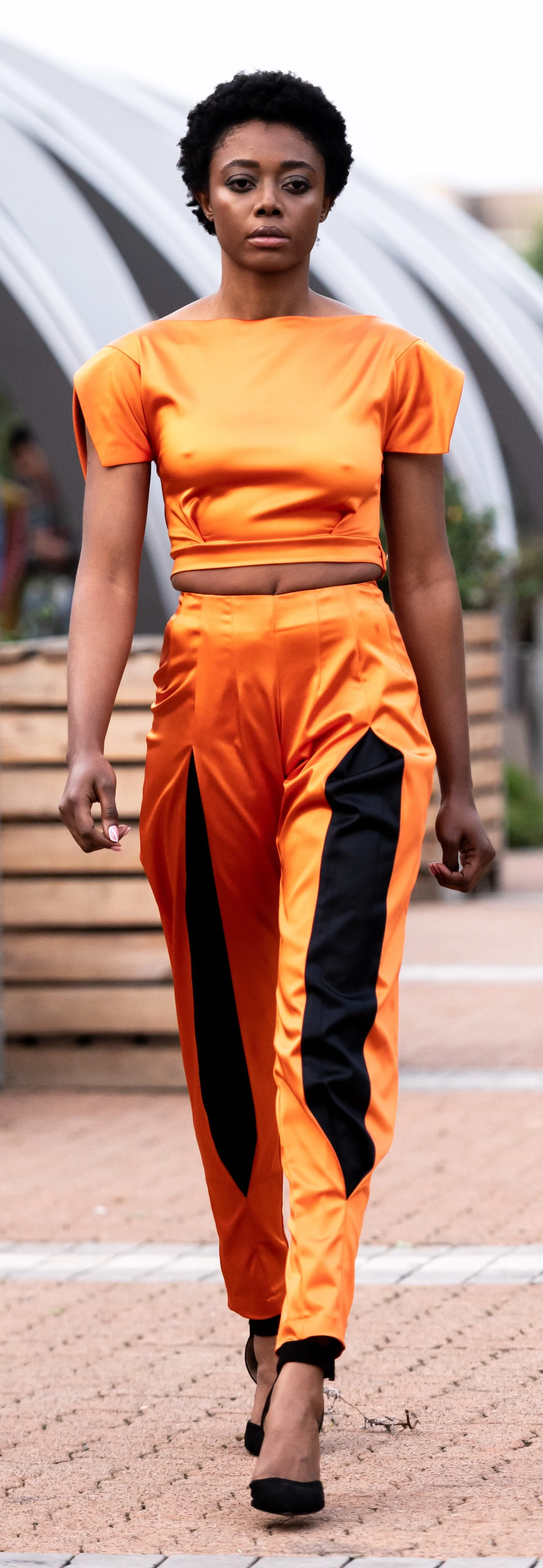 Model walking in orange outfit with black accents on runway