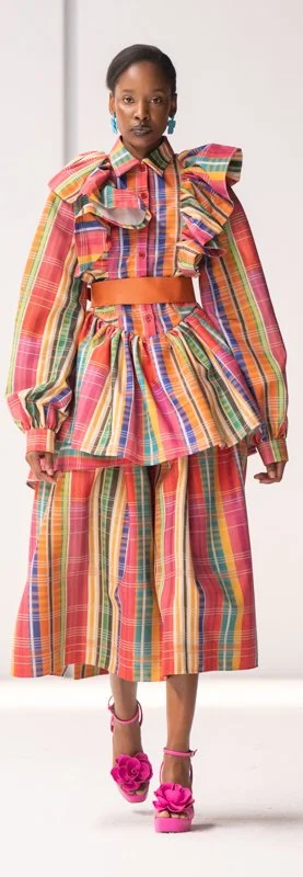 Model wearing a colorful striped outfit with ruffles and pink heels on a runway.