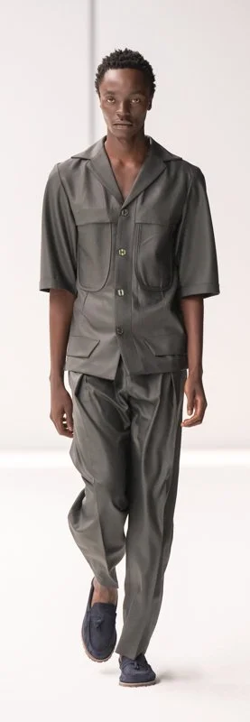Person wearing a gray button-up shirt and trousers on a runway.