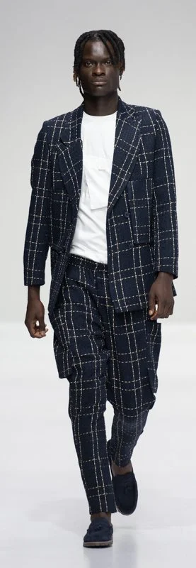 Model wearing a plaid suit with a white shirt on the runway.
