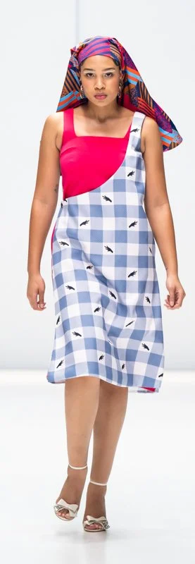 Model in a colorful dress with plaid pattern and bird print, wearing a vibrant headscarf on a runway.
