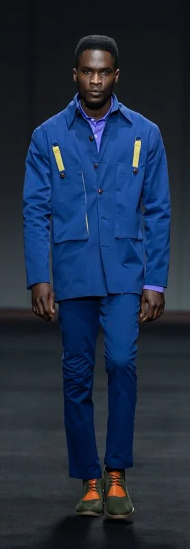 Fashion model wearing blue jacket and pants with orange shoes on runway