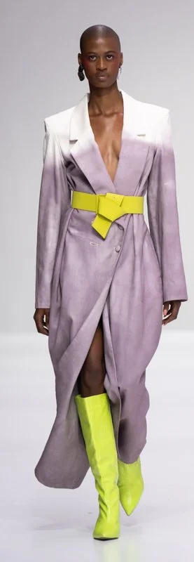 Model wearing a stylish gradient long coat with plunging neckline, a bright yellow belt, and matching yellow neon boots on runway.