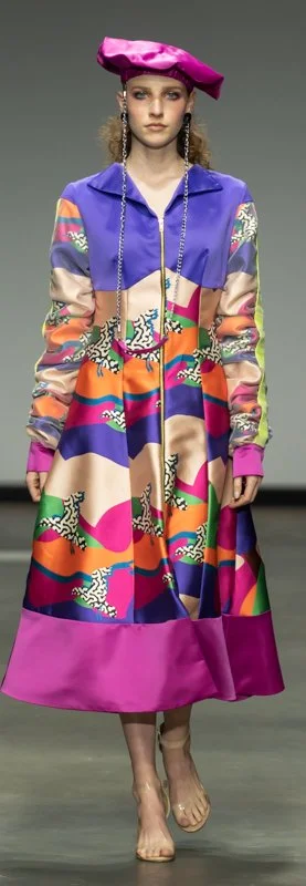 Model wearing a colorful dress and pink beret on a runway.