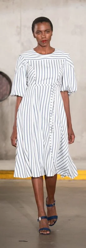 Model wearing a white and blue striped dress with puff sleeves and a belt on a runway.