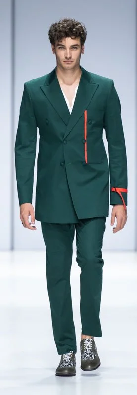 Male model wearing a green double-breasted suit with red accents on the runway